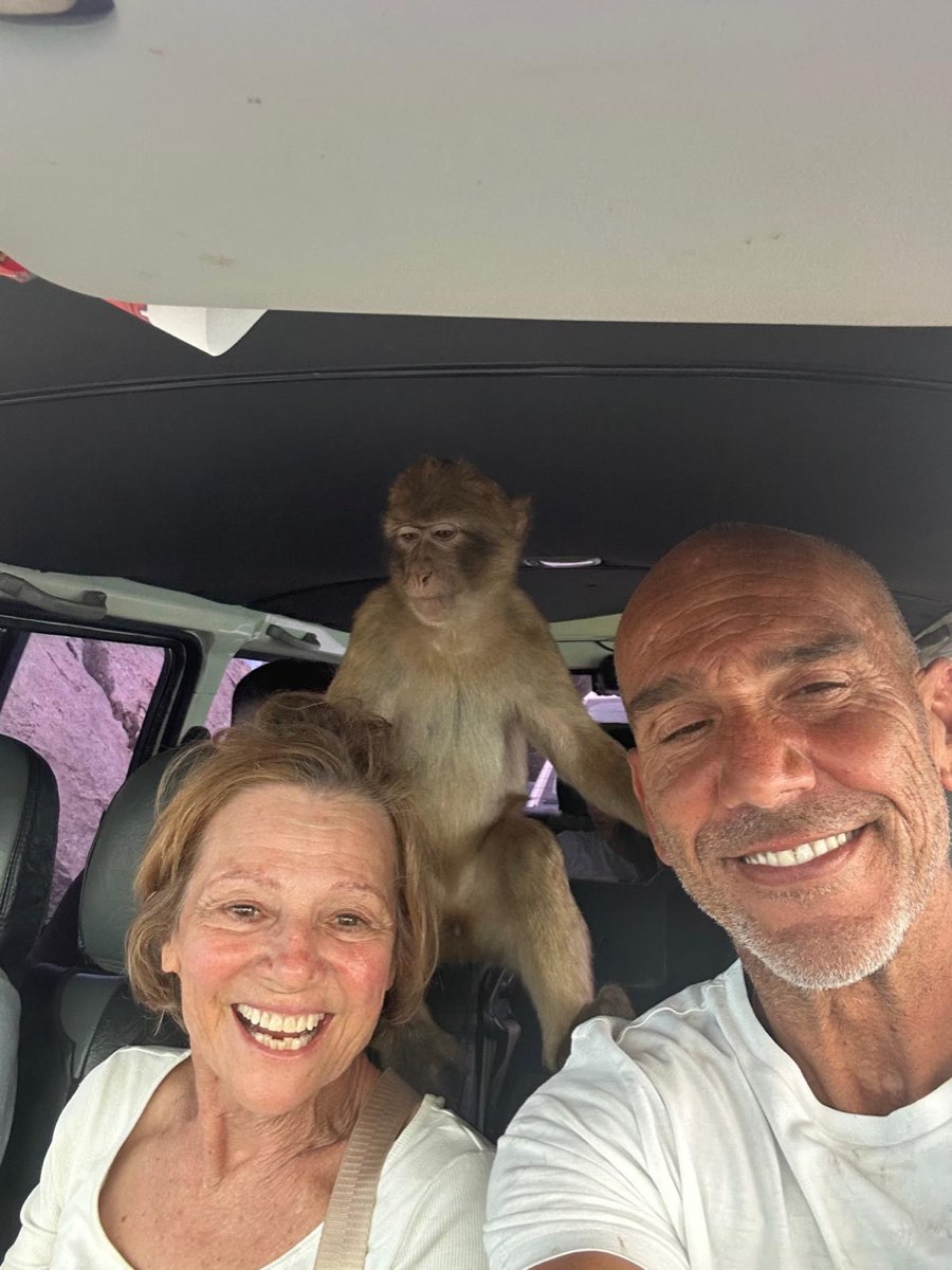 Jason and a smiling guest in the tour vehicle, with a Barbary macaque perched behind them