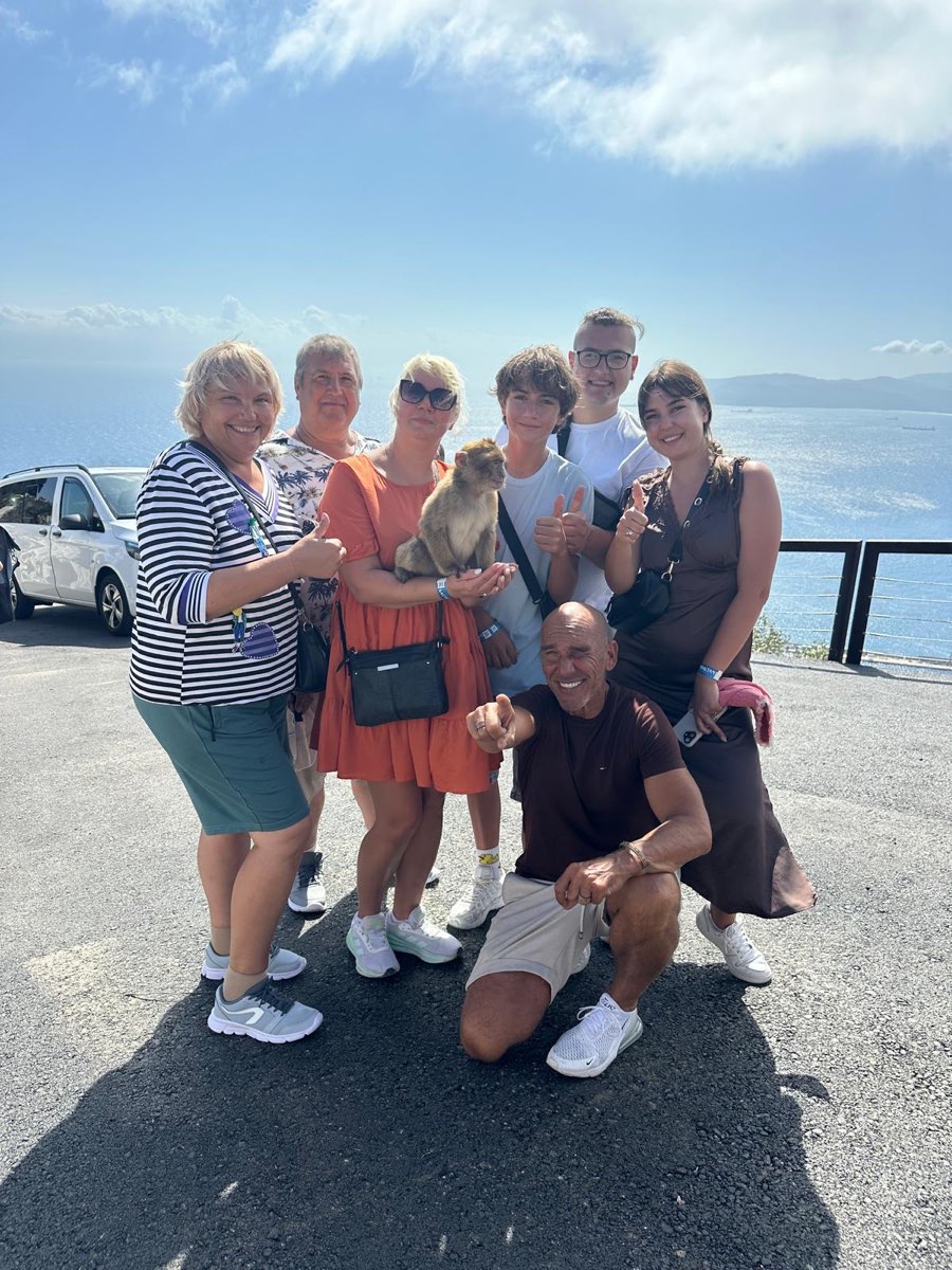 A family tour group with Jason and a Barbary macaque at an Upper Rock viewpoint above the Bay of Gibraltar